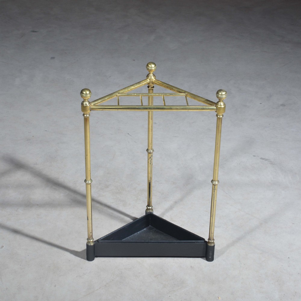 A triangular brass corner stick stand featuring tubular uprights topped with finials and a black cast iron drip tray base. View III