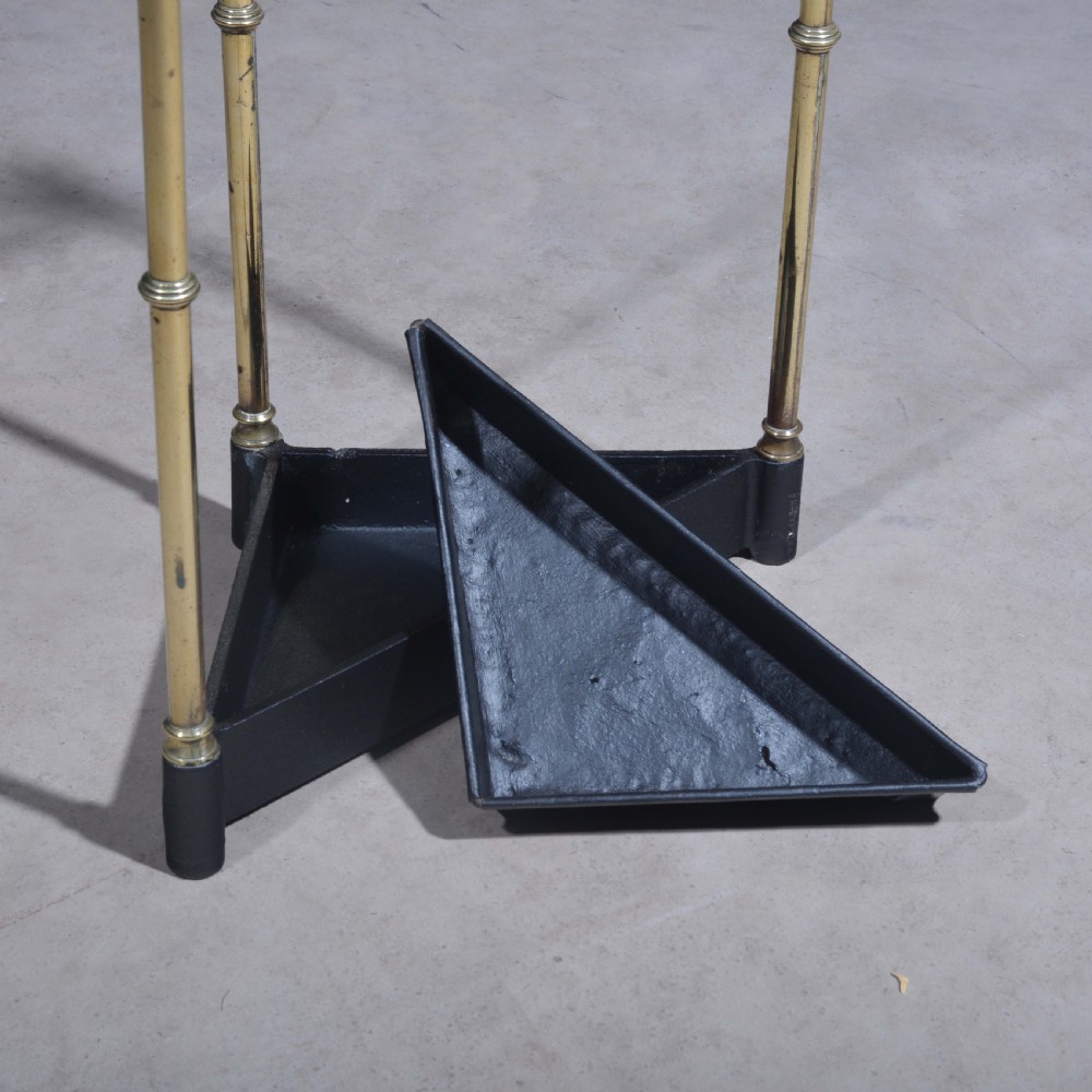 A triangular brass corner stick stand featuring tubular uprights topped with finials and a black cast iron drip tray base. View VI