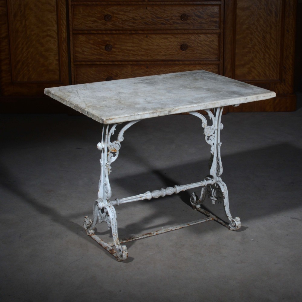 A white painted cast iron table with decorative scrollwork trestle legs and a rectangular grey-veined marble slab top.