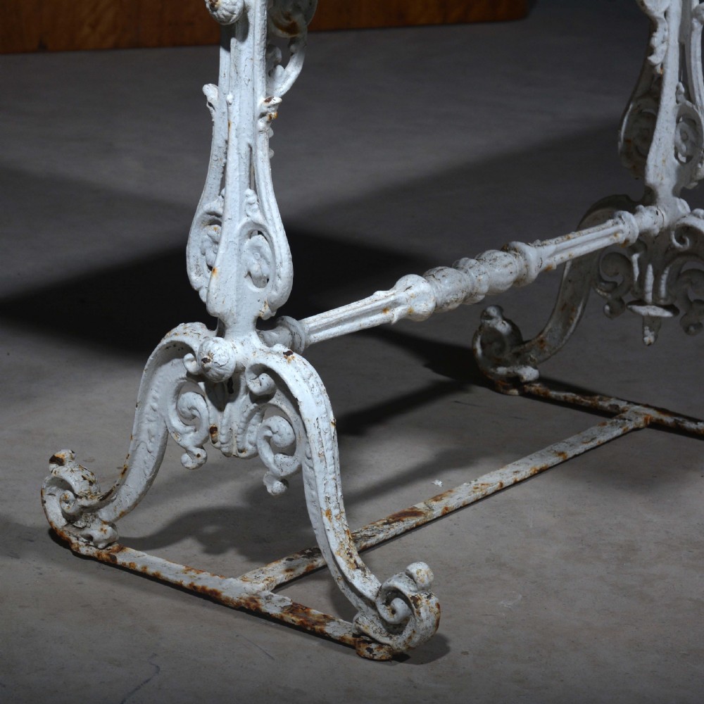A white painted cast iron table with decorative scrollwork trestle legs and a rectangular grey-veined marble slab top. View II