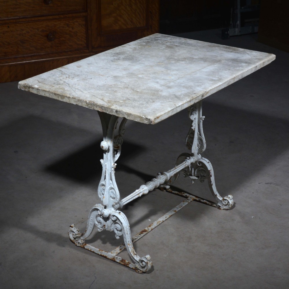 A white painted cast iron table with decorative scrollwork trestle legs and a rectangular grey-veined marble slab top. View III