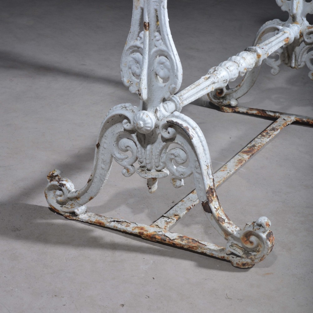 A white painted cast iron table with decorative scrollwork trestle legs and a rectangular grey-veined marble slab top. View IV