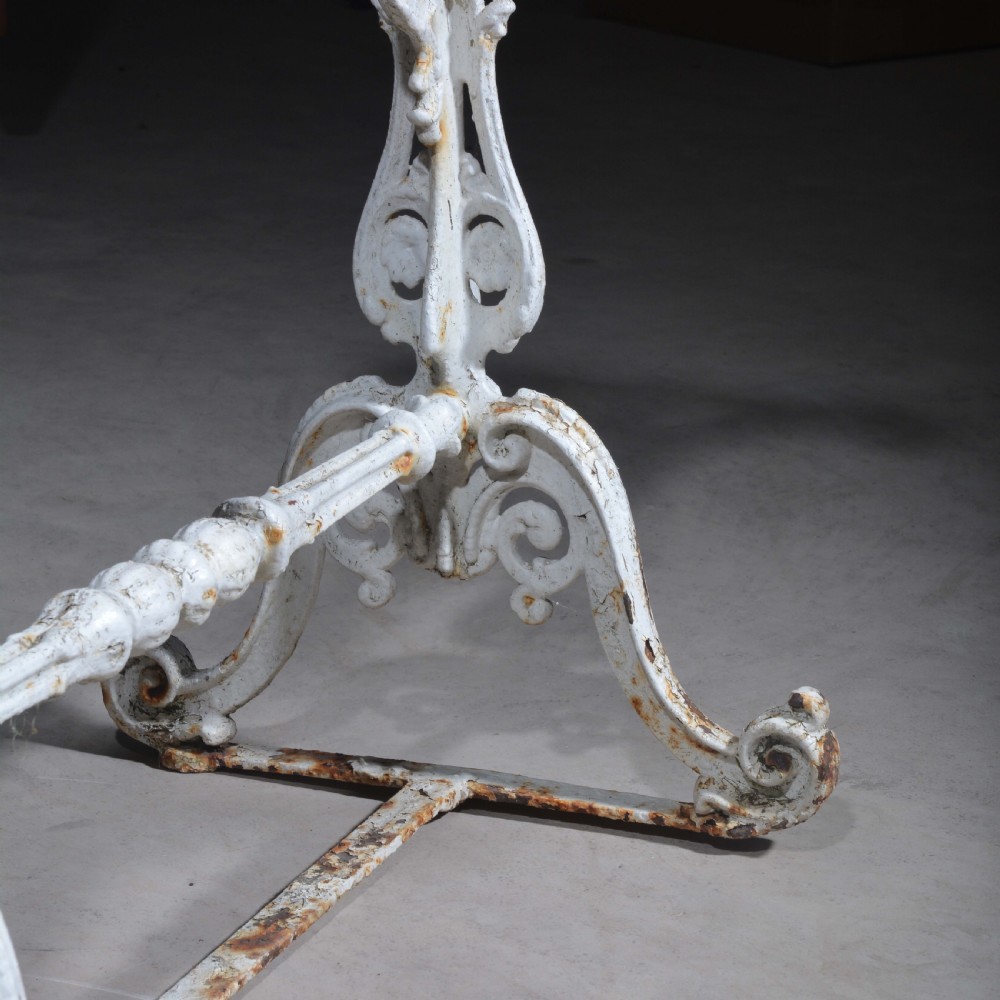 A white painted cast iron table with decorative scrollwork trestle legs and a rectangular grey-veined marble slab top. View V