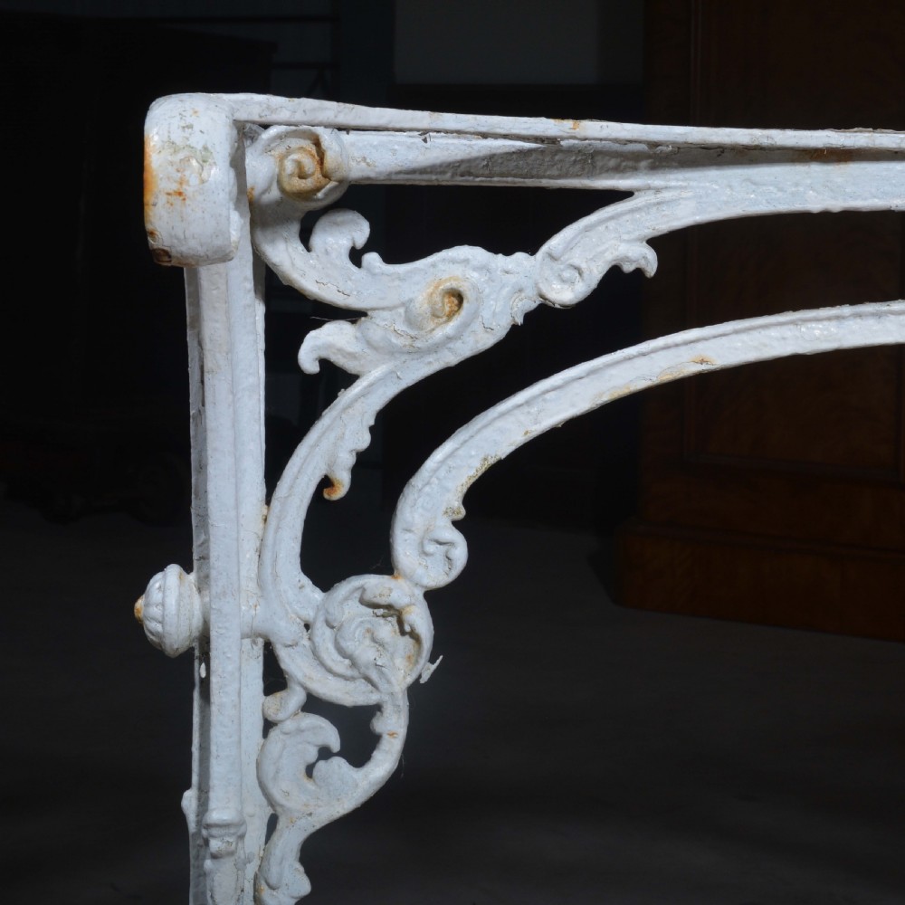 A white painted cast iron table with decorative scrollwork trestle legs and a rectangular grey-veined marble slab top. View VII