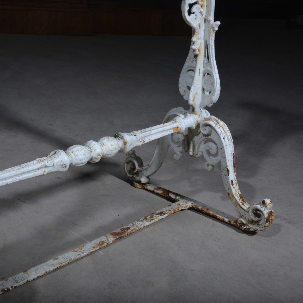 A white painted cast iron table with decorative scrollwork trestle legs and a rectangular grey-veined marble slab top. View VIII