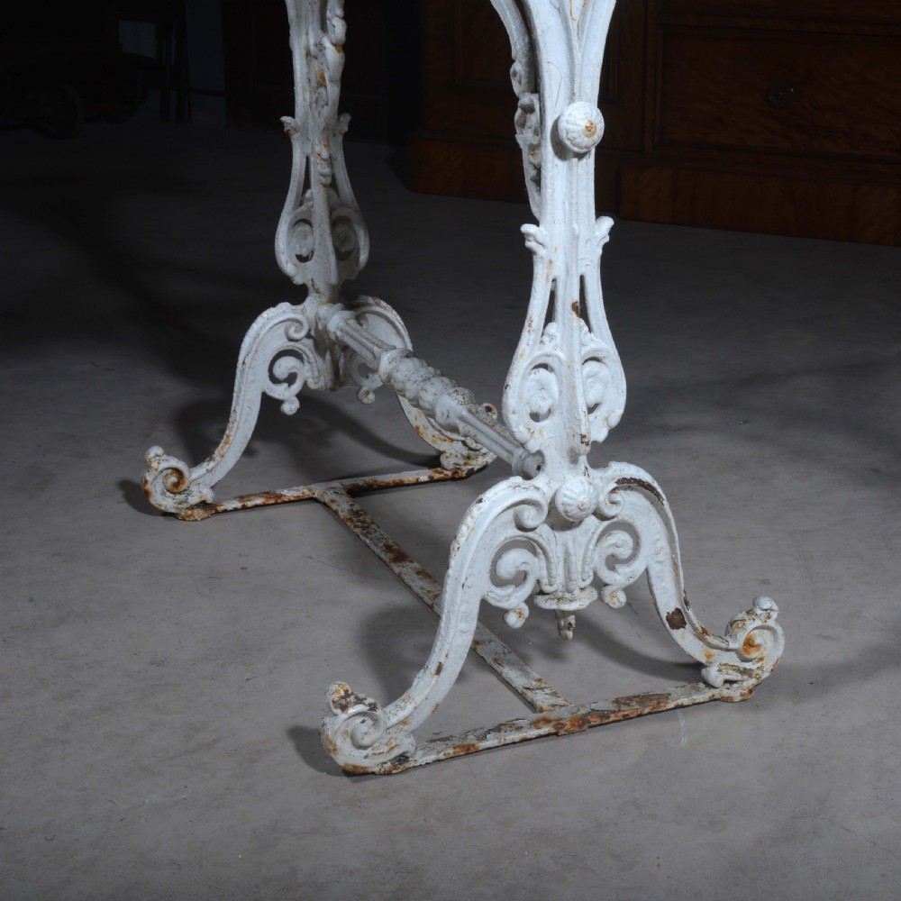 A white painted cast iron table with decorative scrollwork trestle legs and a rectangular grey-veined marble slab top. View IX