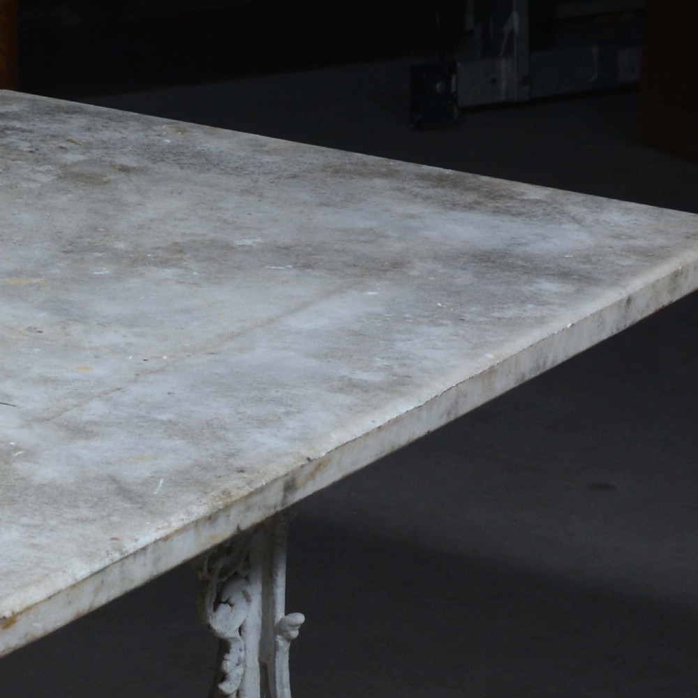 A white painted cast iron table with decorative scrollwork trestle legs and a rectangular grey-veined marble slab top. View X