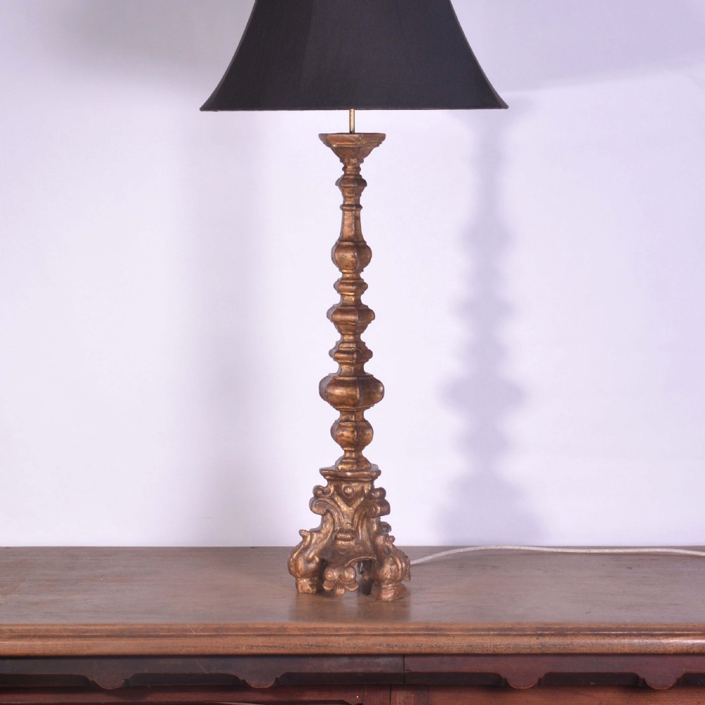 A tall Spanish gilt wood table lamp featuring a turned, carved column base finished in gold leaf, paired with a black flared lampshade.