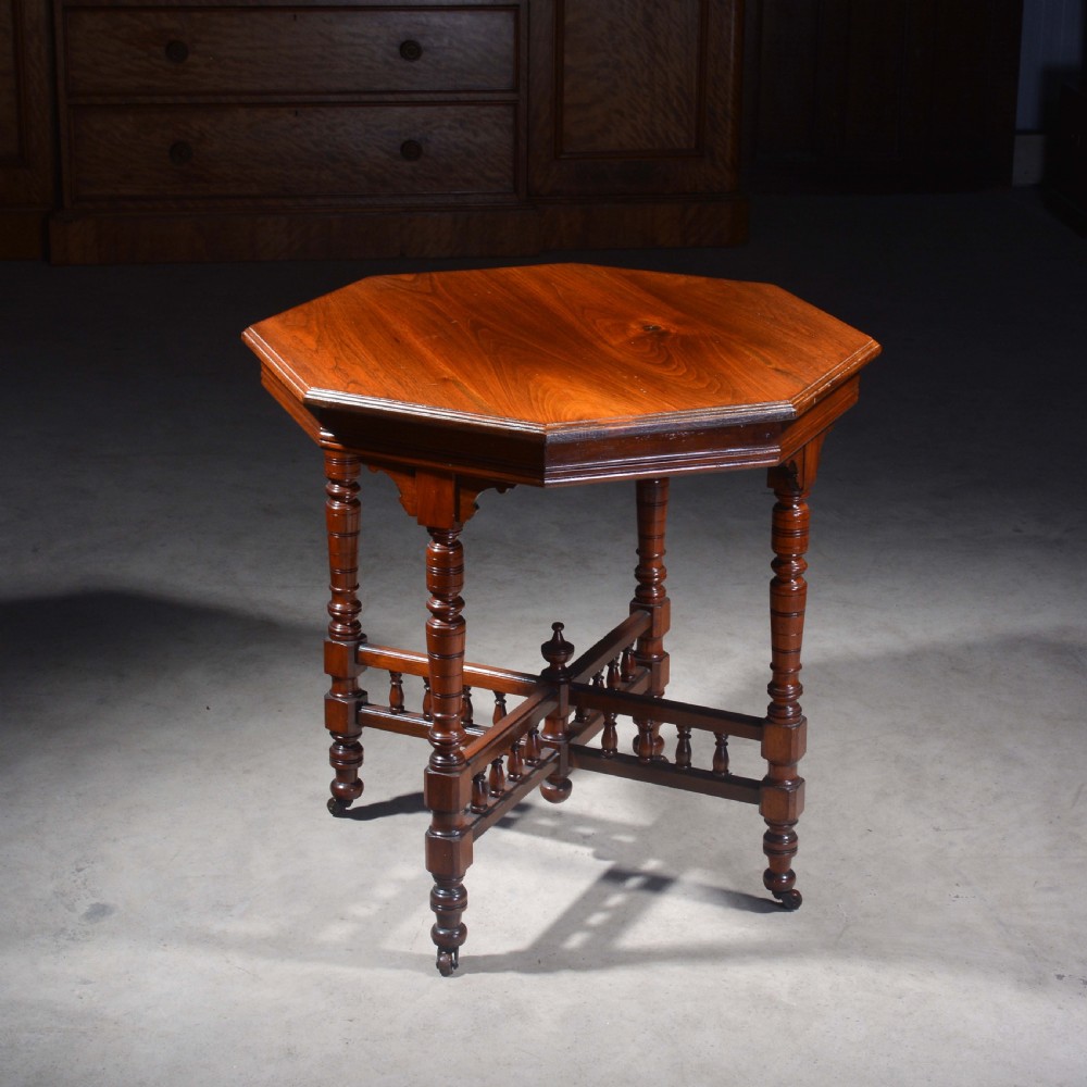 An Victorian octagonal top occasional table in polished dark walnut featuring turned legs, a spindled cross-stretcher, and brass castors.