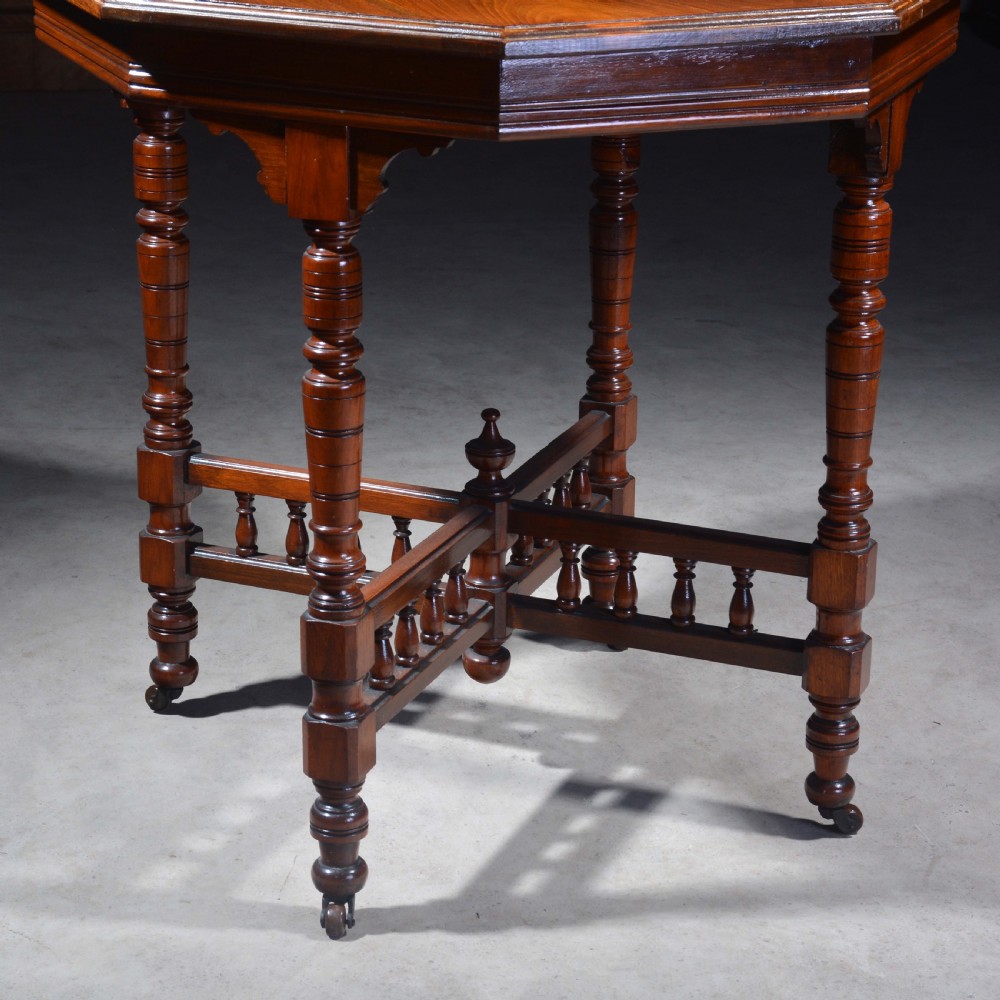 An Victorian octagonal top occasional table in polished dark walnut featuring turned legs, a spindled cross-stretcher, and brass castors. View II