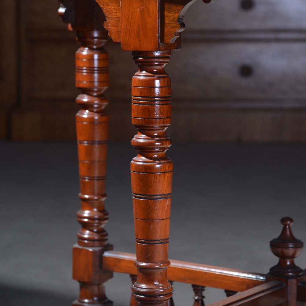 An Victorian octagonal top occasional table in polished dark walnut featuring turned legs, a spindled cross-stretcher, and brass castors. View III