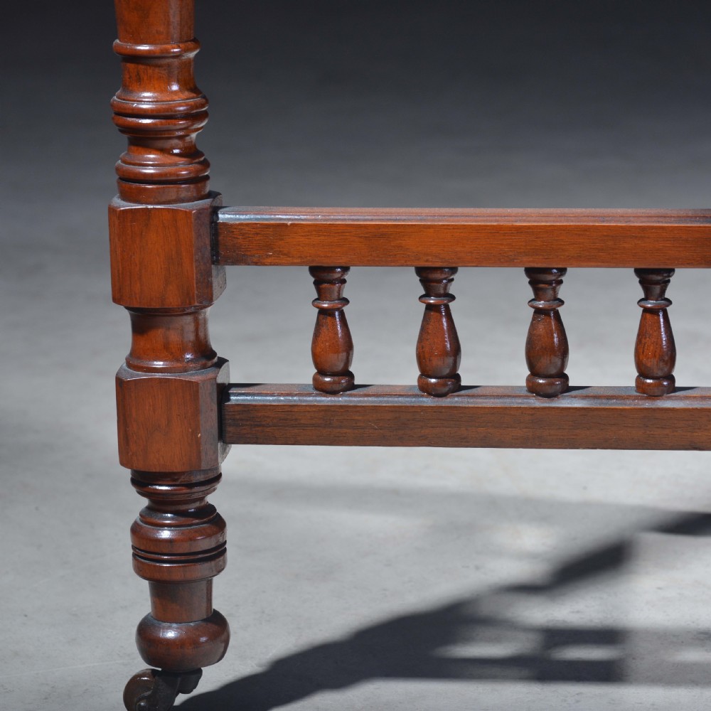 An Victorian octagonal top occasional table in polished dark walnut featuring turned legs, a spindled cross-stretcher, and brass castors. View V