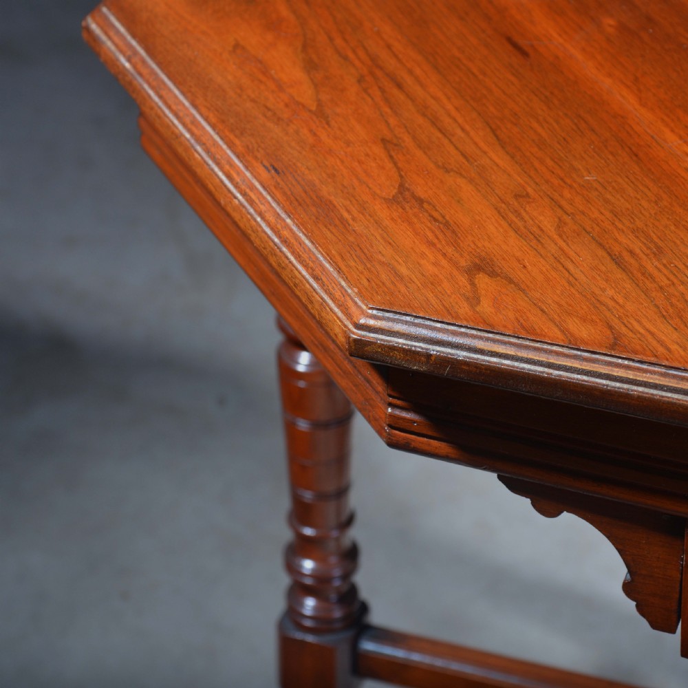 An Victorian octagonal top occasional table in polished dark walnut featuring turned legs, a spindled cross-stretcher, and brass castors. View VI