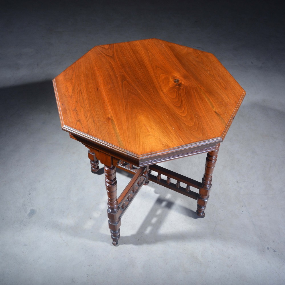 An Victorian octagonal top occasional table in polished dark walnut featuring turned legs, a spindled cross-stretcher, and brass castors. View VII