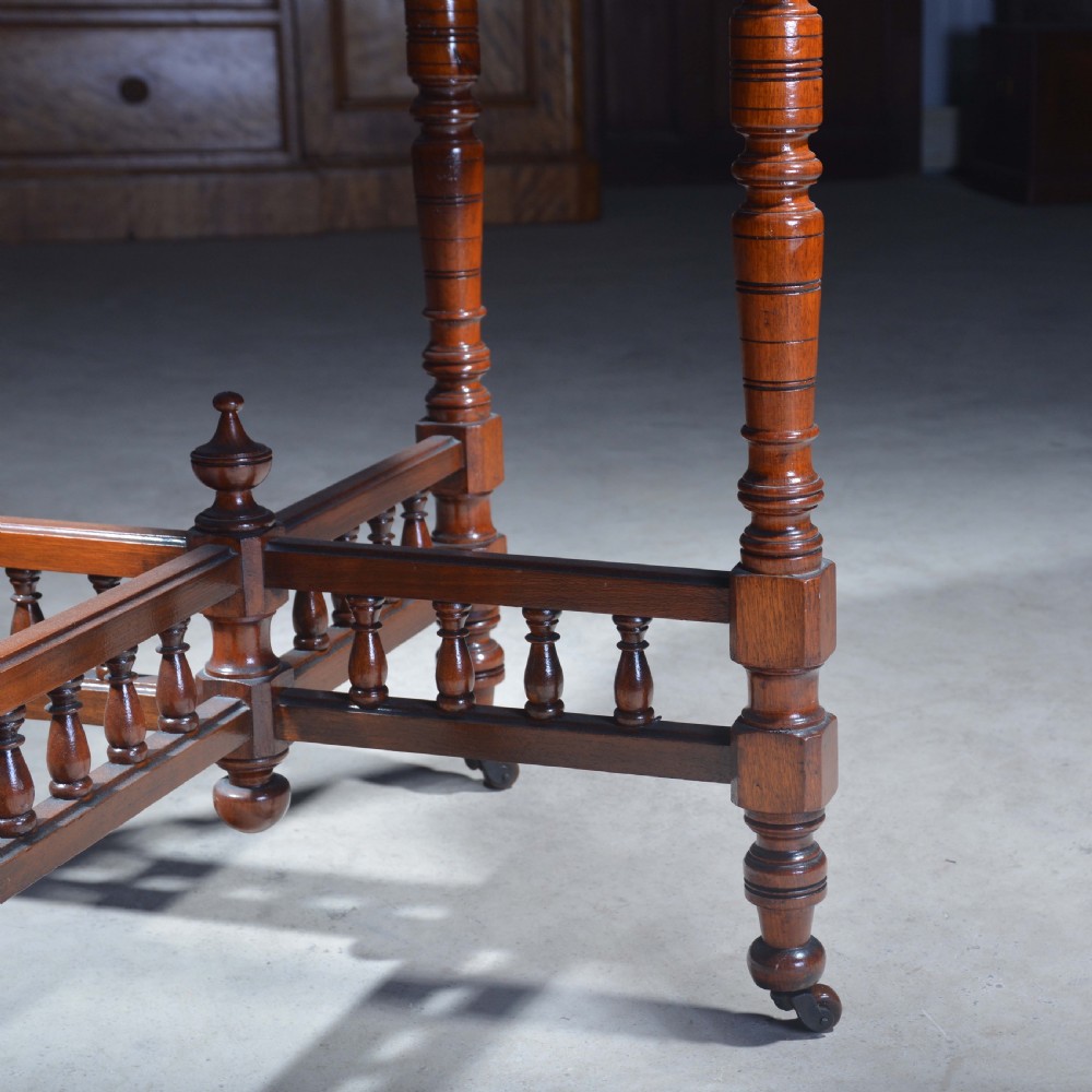 An Victorian octagonal top occasional table in polished dark walnut featuring turned legs, a spindled cross-stretcher, and brass castors. View VIII