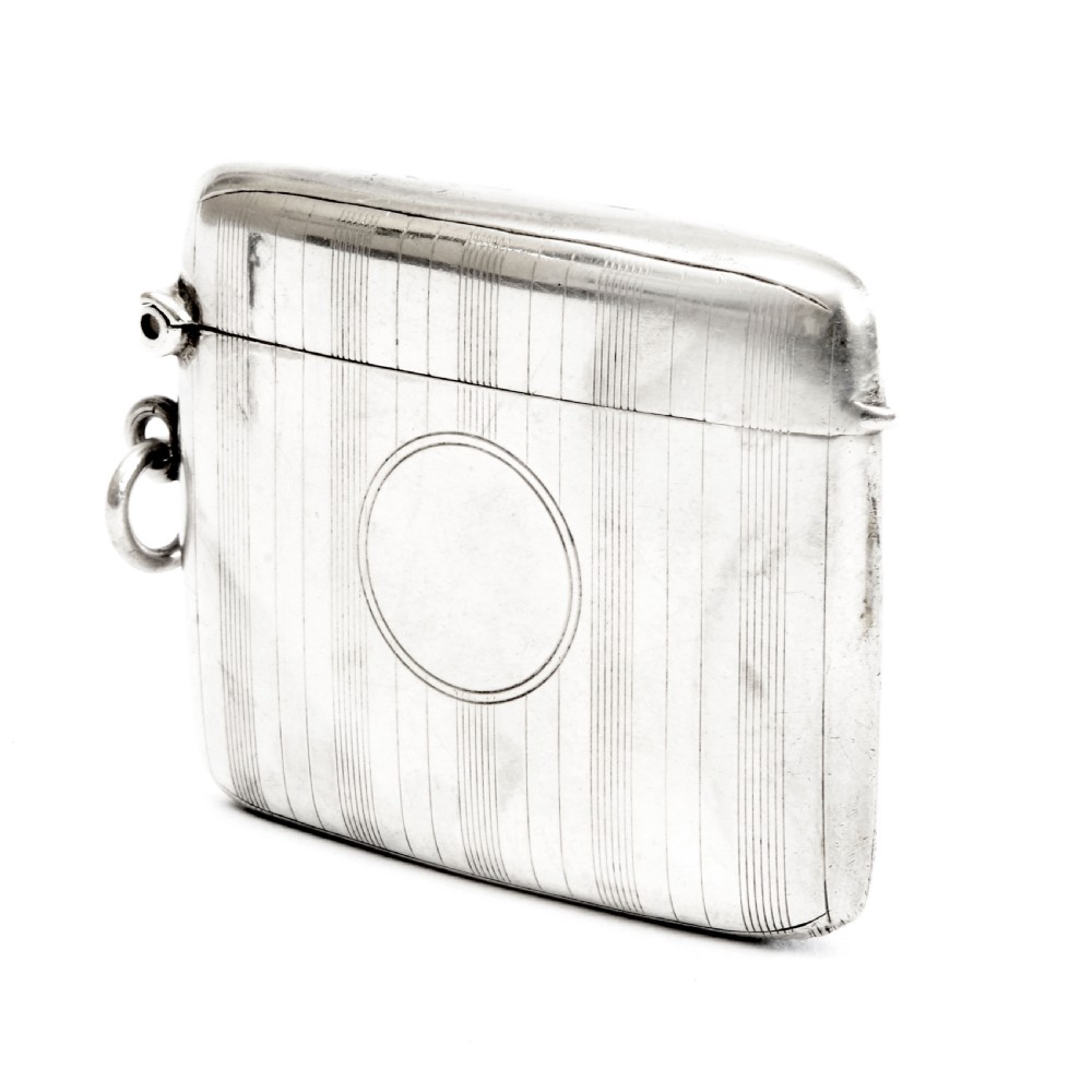 An engine-turned sterling silver vesta case with a circular unengraved cartouche, hinged lid, and side suspension loop against a plain background.
