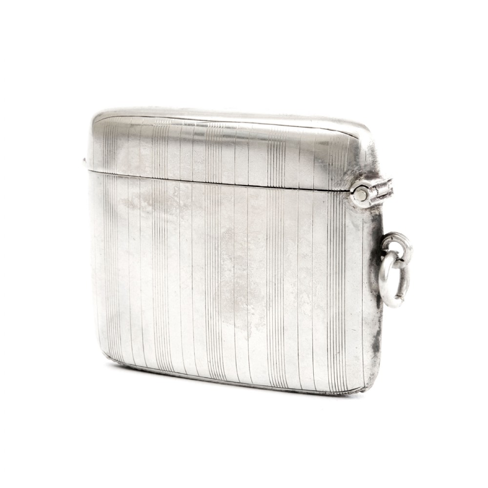 An engine-turned sterling silver vesta case with a circular unengraved cartouche, hinged lid, and side suspension loop against a plain background. View II