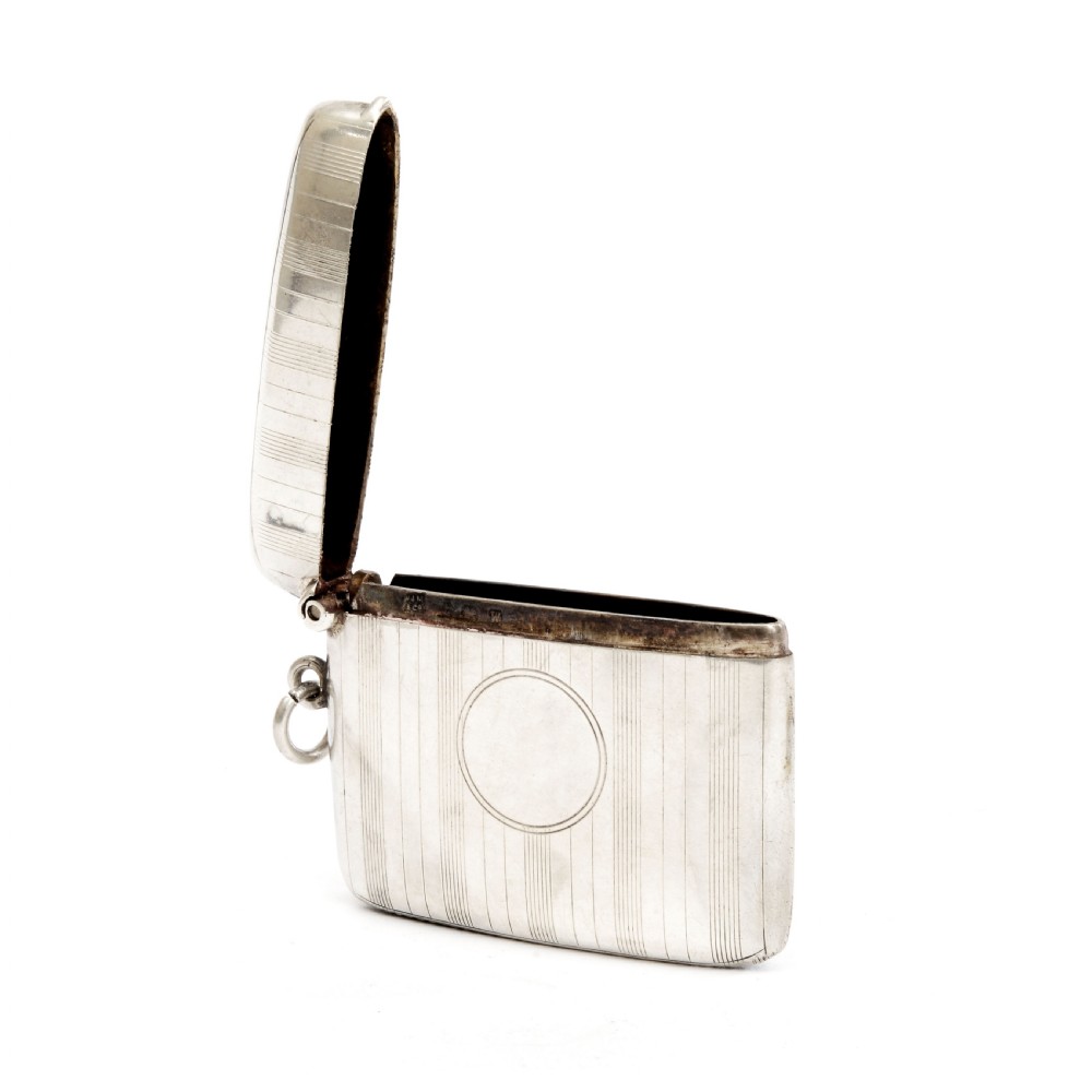 An engine-turned sterling silver vesta case with a circular unengraved cartouche, hinged lid, and side suspension loop against a plain background. View III