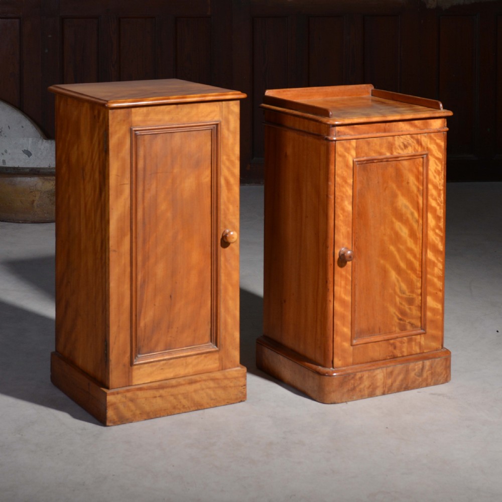 A near pair of Victorian satin birch bedside cabinets featuring single panelled doors, turned timber knobs, and plinth bases.