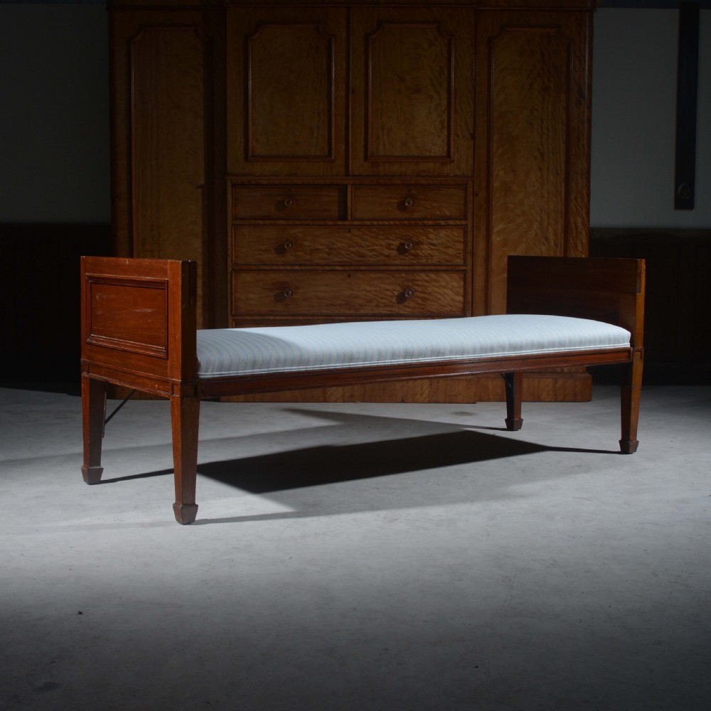 An antique mahogany day bed with panelled endboards, tapered square legs, and a striped light blue upholstered mattress cushion.
