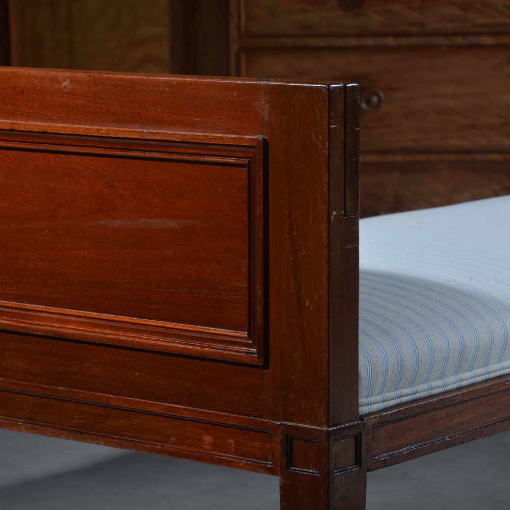 An antique mahogany day bed with panelled endboards, tapered square legs, and a striped light blue upholstered mattress cushion. View II