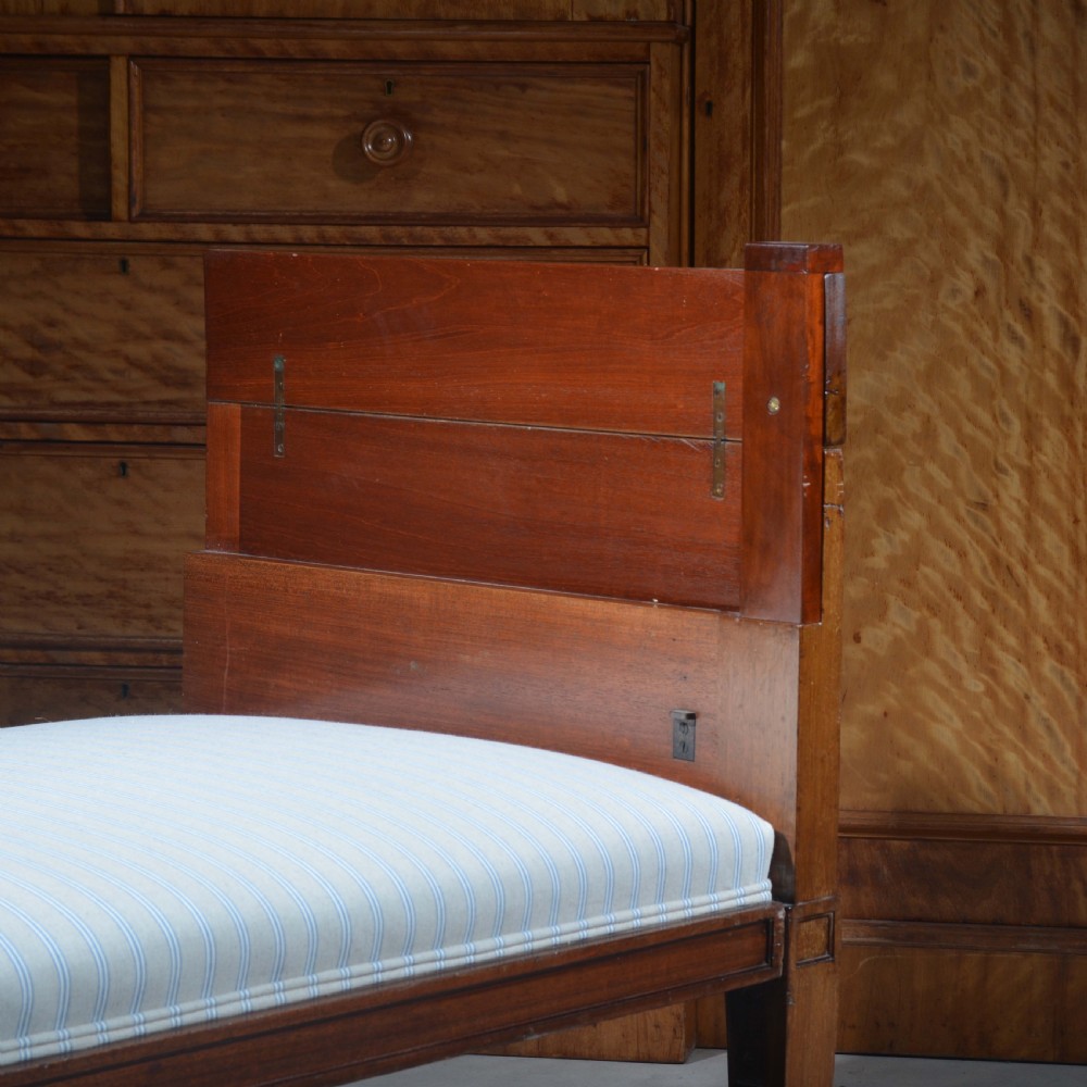 An antique mahogany day bed with panelled endboards, tapered square legs, and a striped light blue upholstered mattress cushion. View III
