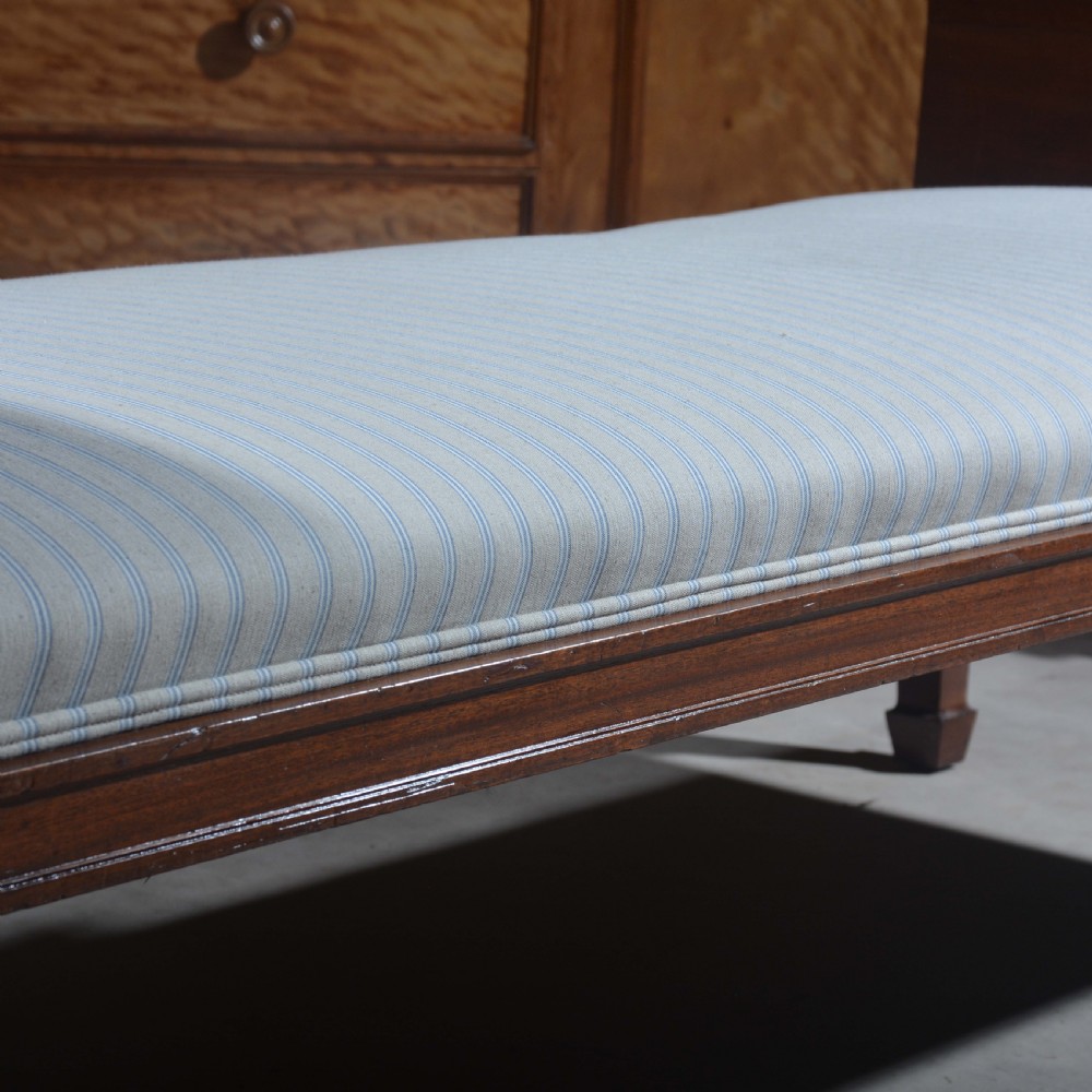 An antique mahogany day bed with panelled endboards, tapered square legs, and a striped light blue upholstered mattress cushion. View V