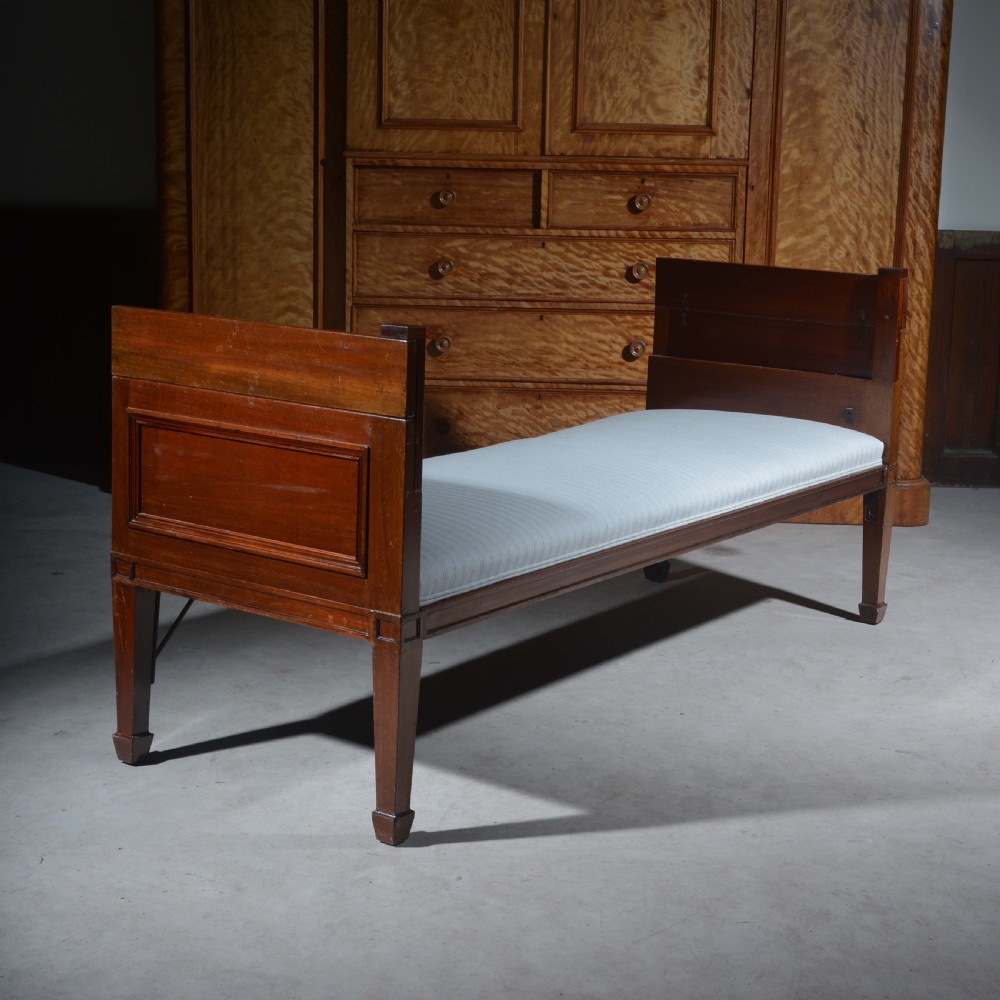 An antique mahogany day bed with panelled endboards, tapered square legs, and a striped light blue upholstered mattress cushion. View VIII