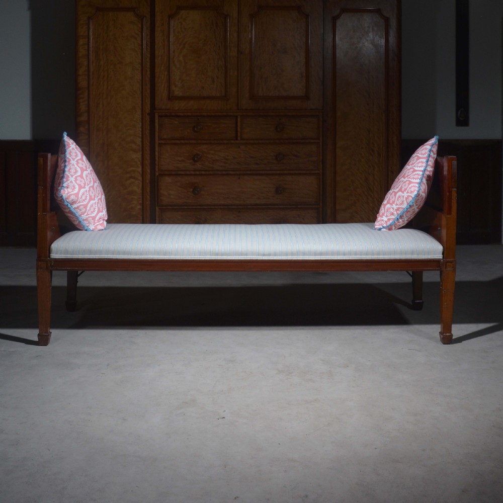 An antique mahogany day bed with panelled endboards, tapered square legs, and a striped light blue upholstered mattress cushion. View IX