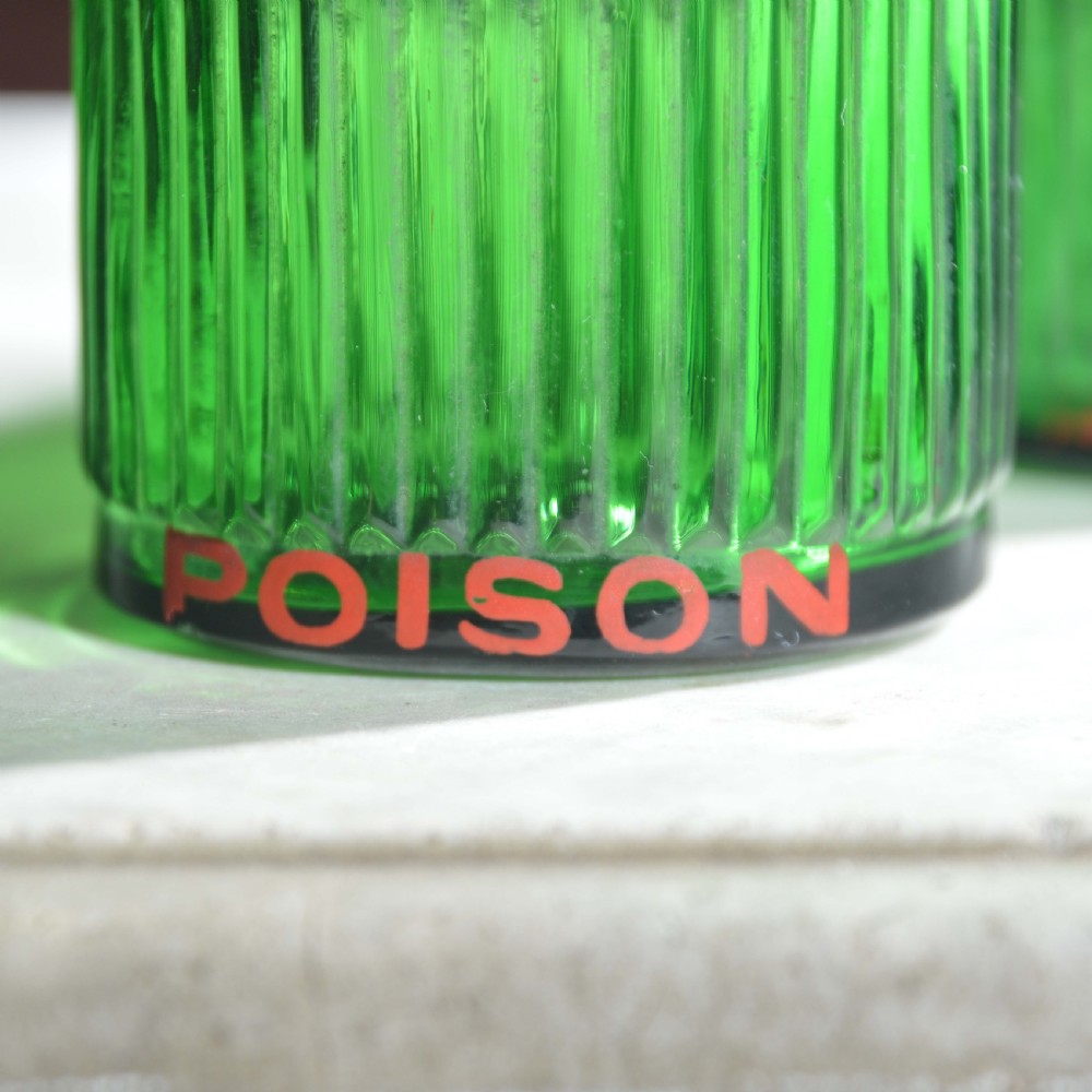 A row of five ribbed emerald green glass apothecary bottles with ground glass stoppers and red gilt-edged labels. View IX