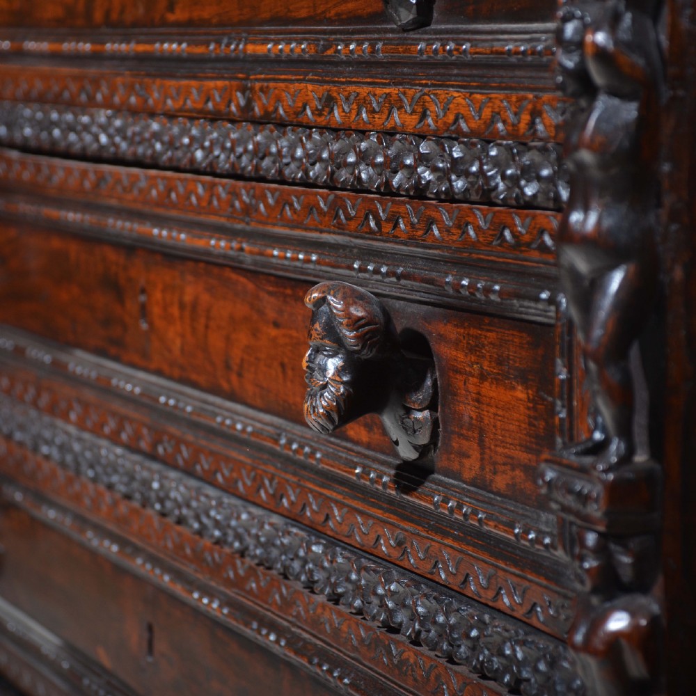 A dark carved walnut Italian Renaissance style chest of drawers featuring small carved figural pilasters and turned bun feet. View VI