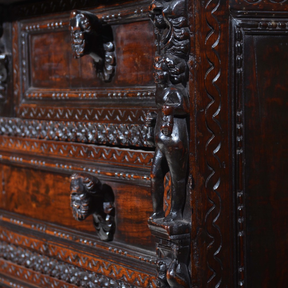 A dark carved walnut Italian Renaissance style chest of drawers featuring small carved figural pilasters and turned bun feet. View VII