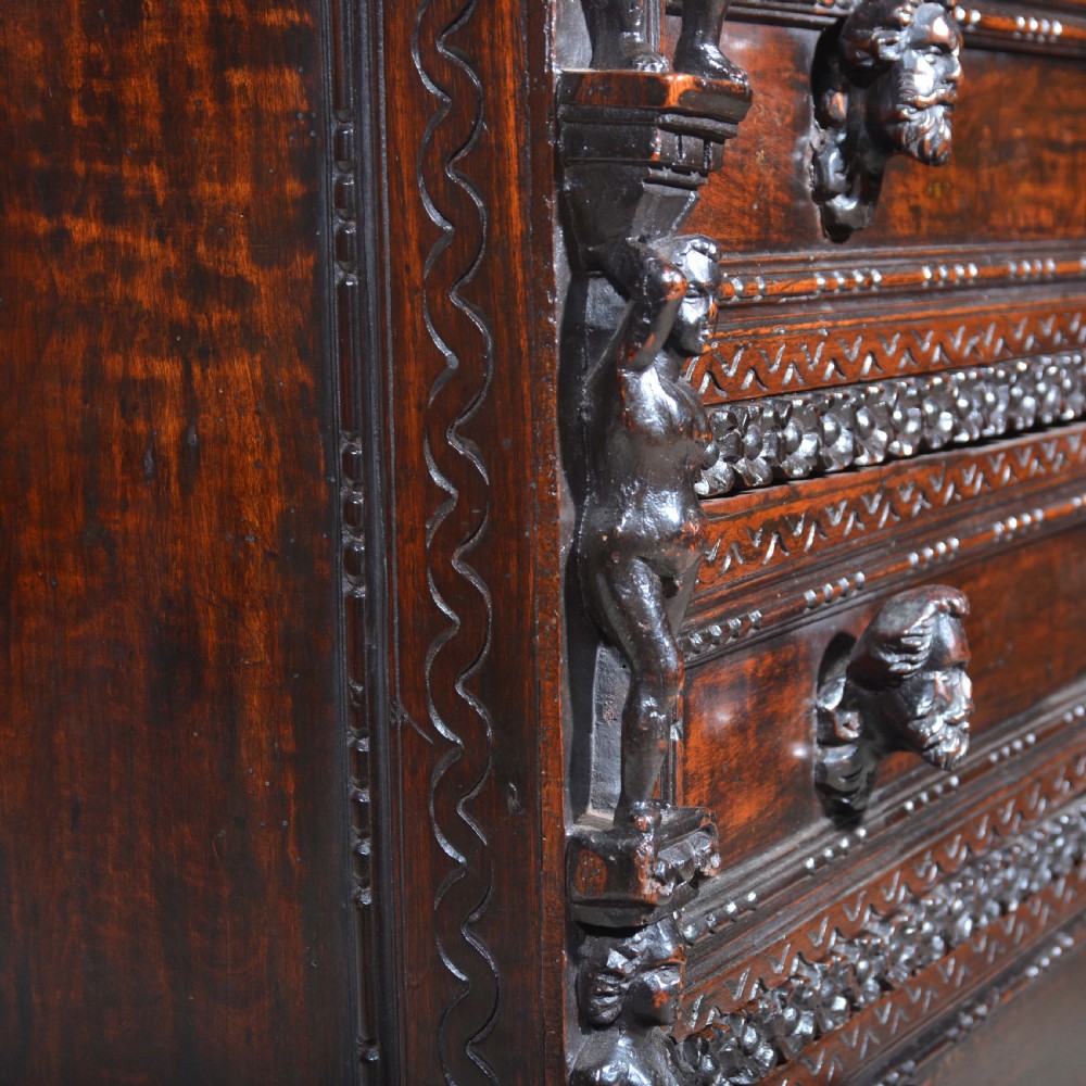 A dark carved walnut Italian Renaissance style chest of drawers featuring small carved figural pilasters and turned bun feet. View XII