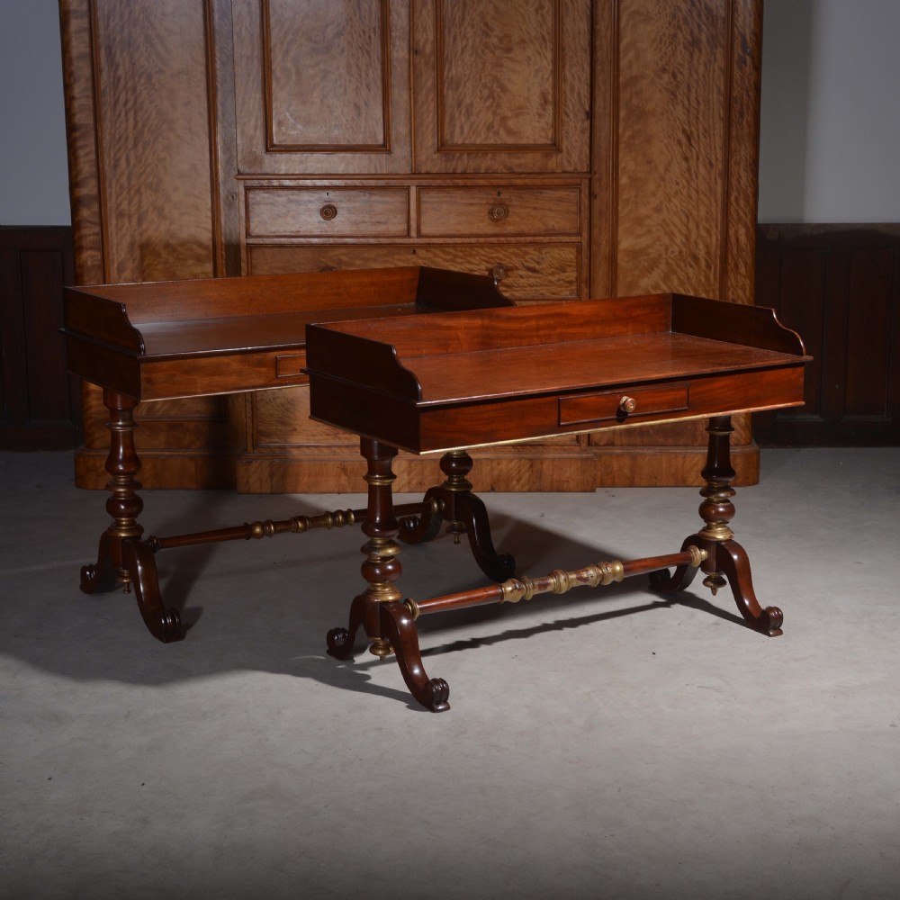 A matched pair of mahogany dressing tables featuring raised gallery tops, single frieze drawers, and turned legs with brass-collared stretchers.