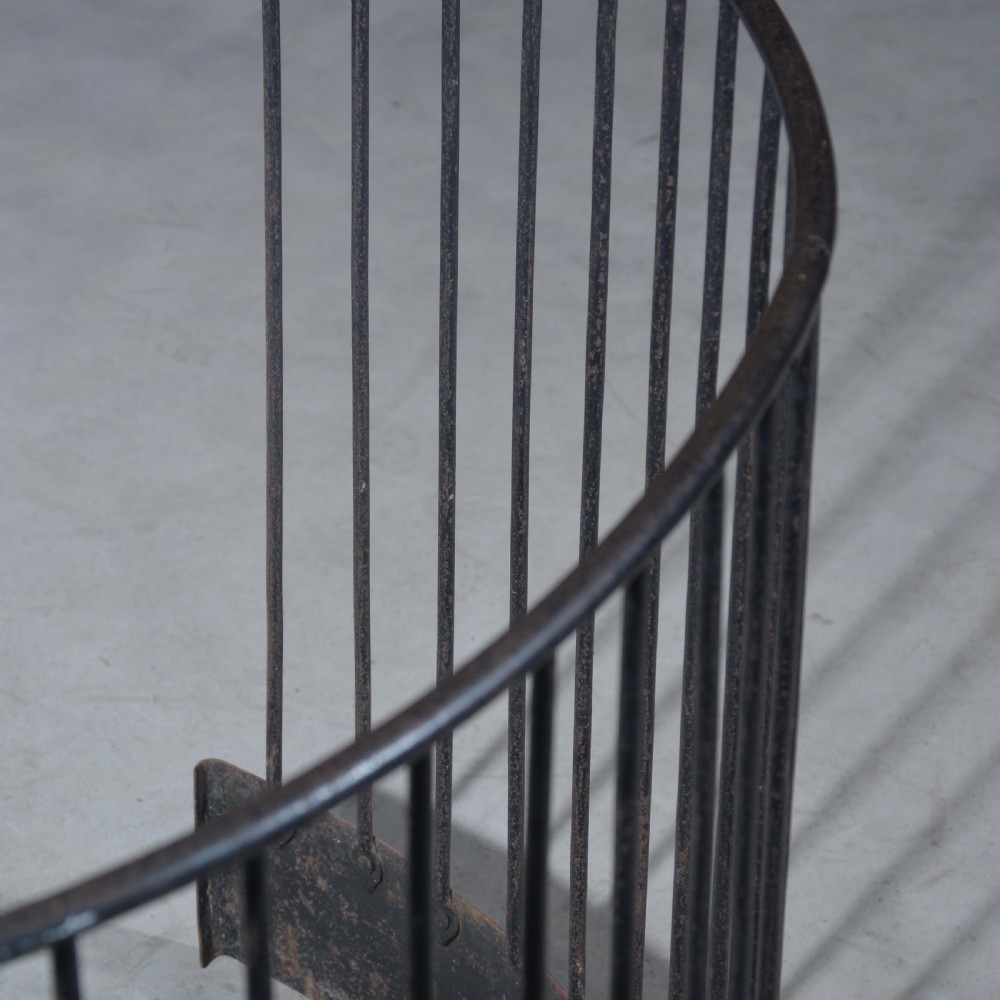 A curved wrought iron nursery fender with closely spaced vertical bars mounted onto a solid metal plinth base. View III