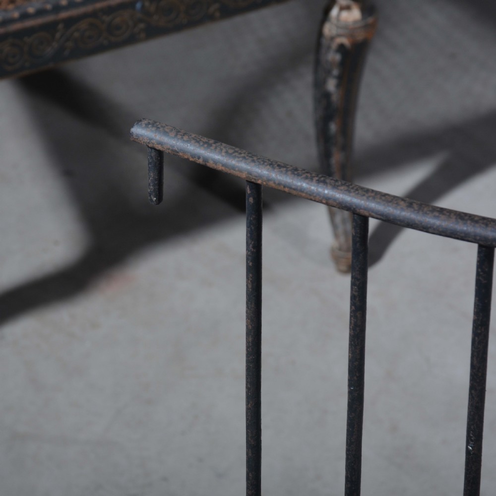 A curved wrought iron nursery fender with closely spaced vertical bars mounted onto a solid metal plinth base. View V