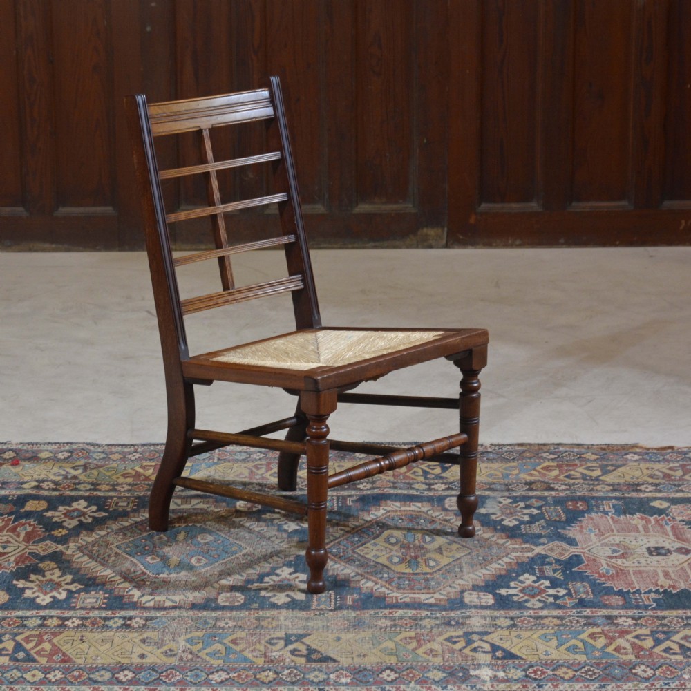 An antique dark oak Aesthetic Movement low side chair featuring a woven rush seat and a slotted backrest with turned legs.