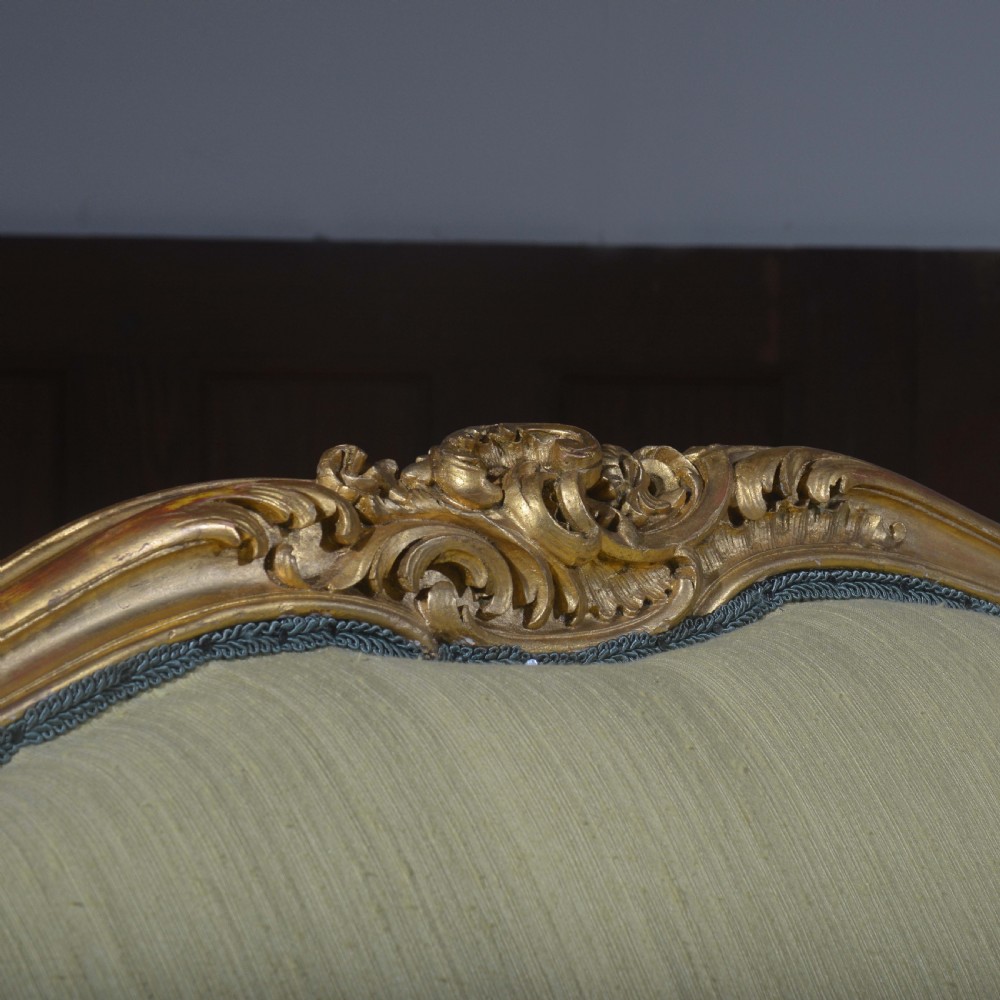 A French Louis XV style giltwood settee featuring a curved carved frame, cabriole legs, and light yellow fabric upholstery with blue trim. View II