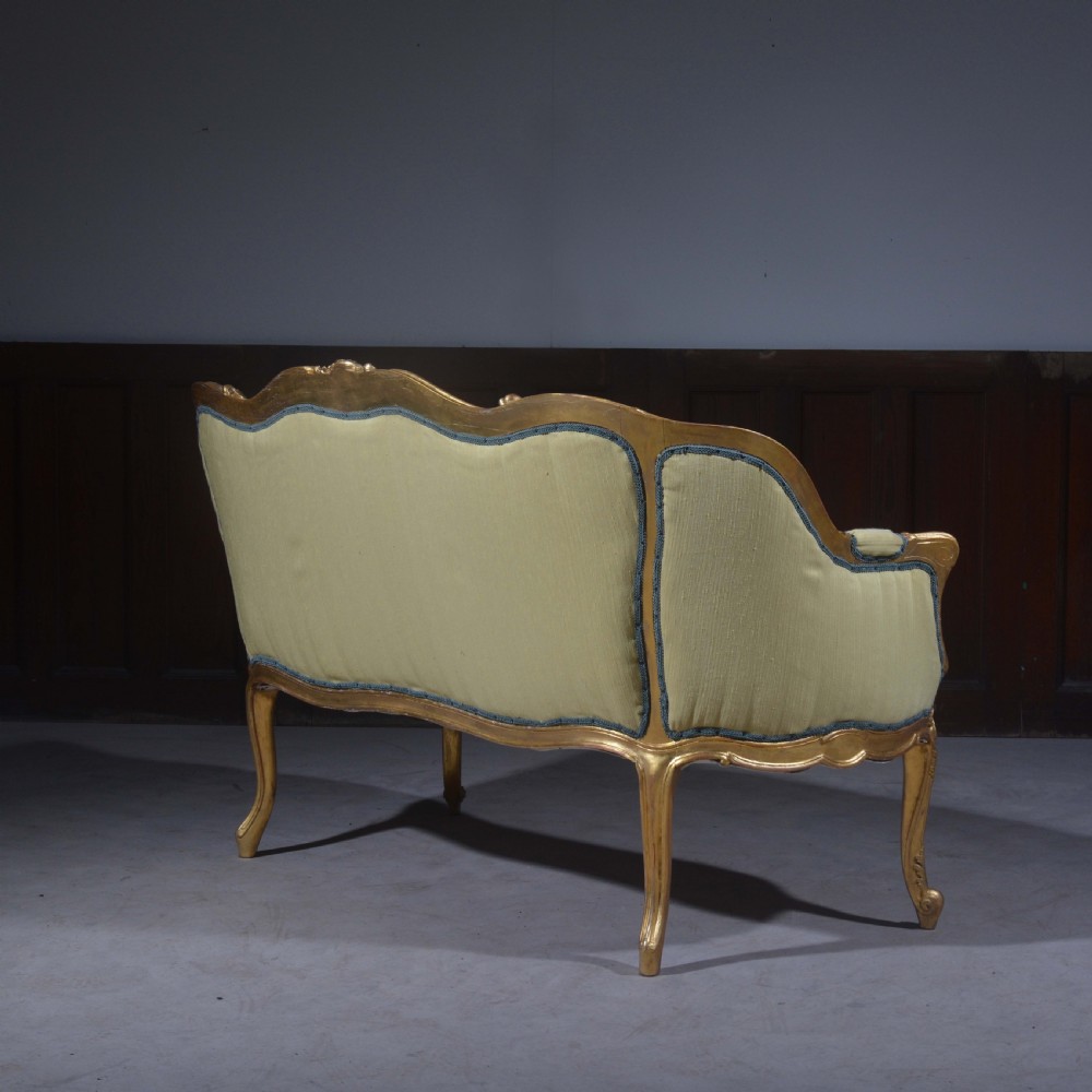 A French Louis XV style giltwood settee featuring a curved carved frame, cabriole legs, and light yellow fabric upholstery with blue trim. View III