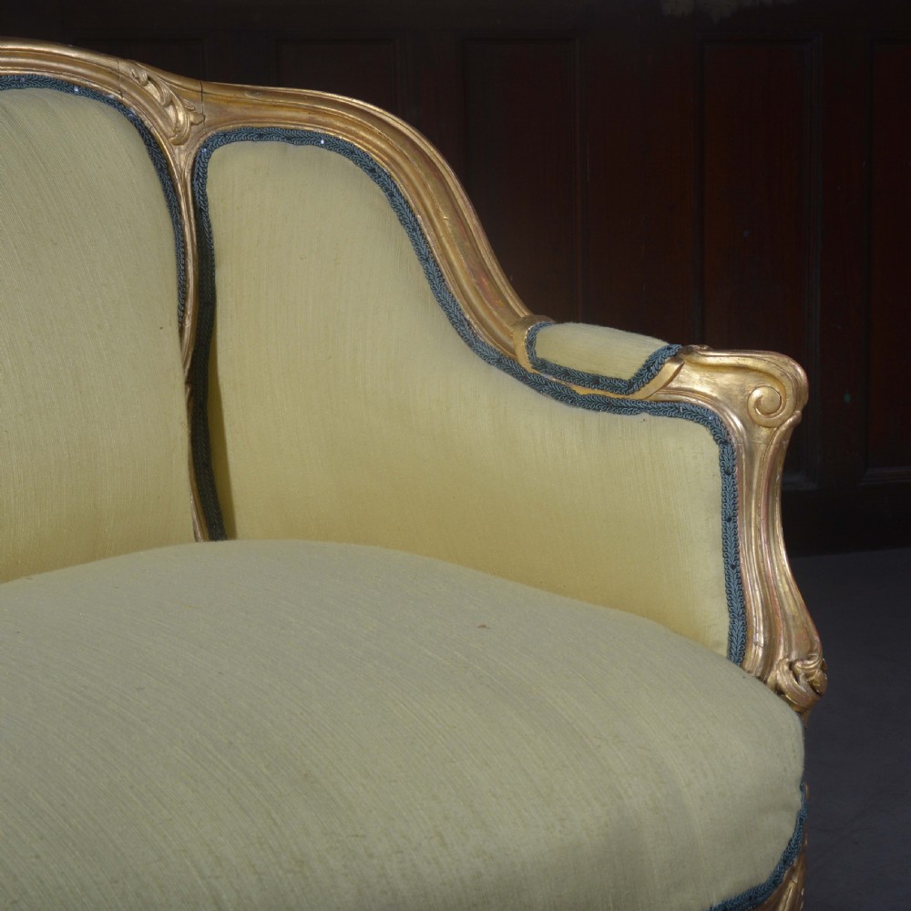 A French Louis XV style giltwood settee featuring a curved carved frame, cabriole legs, and light yellow fabric upholstery with blue trim. View V