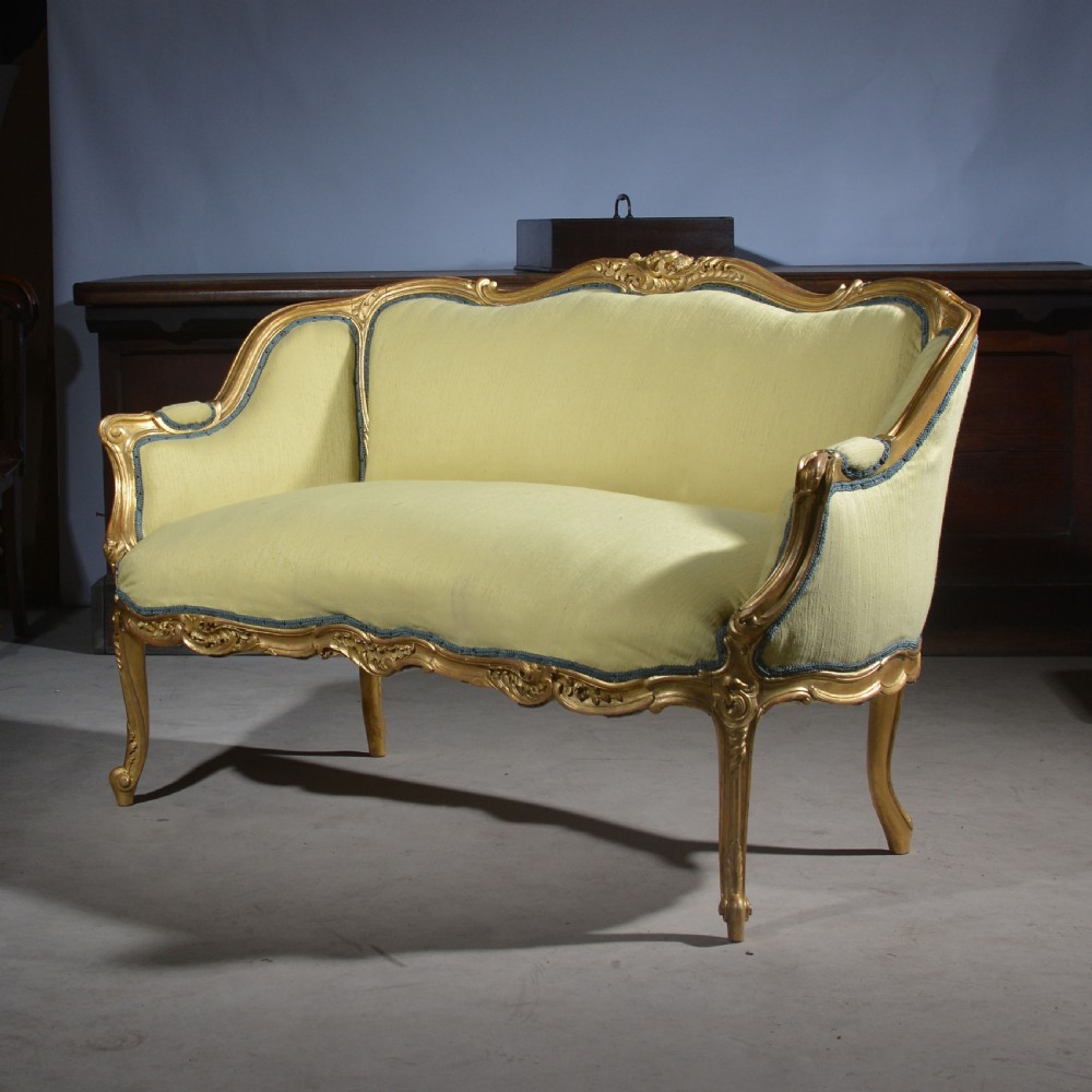 A French Louis XV style giltwood settee featuring a curved carved frame, cabriole legs, and light yellow fabric upholstery with blue trim. View VI