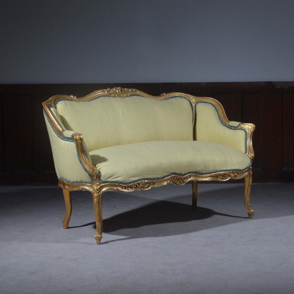 A French Louis XV style giltwood settee featuring a curved carved frame, cabriole legs, and light yellow fabric upholstery with blue trim. View VII