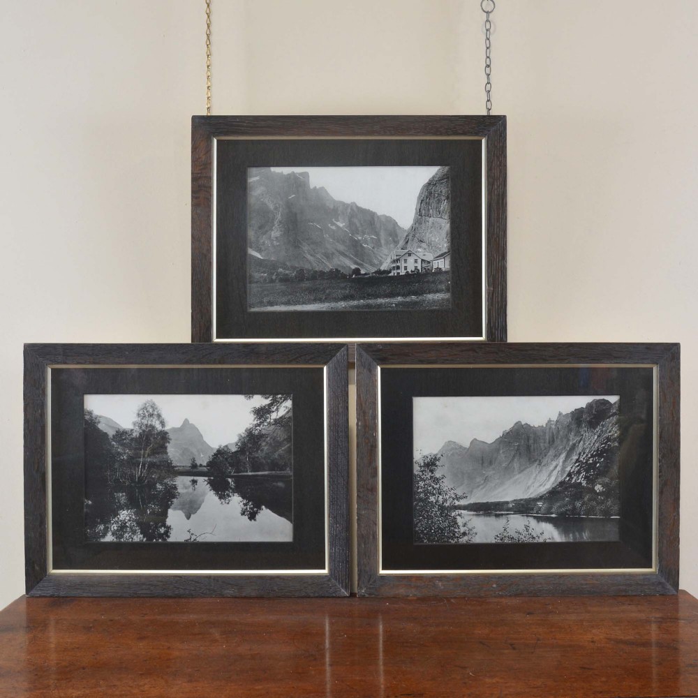 Set of three dark oak framed monochrome photographs featuring Alpine mountain views, chalets, and lake reflections.