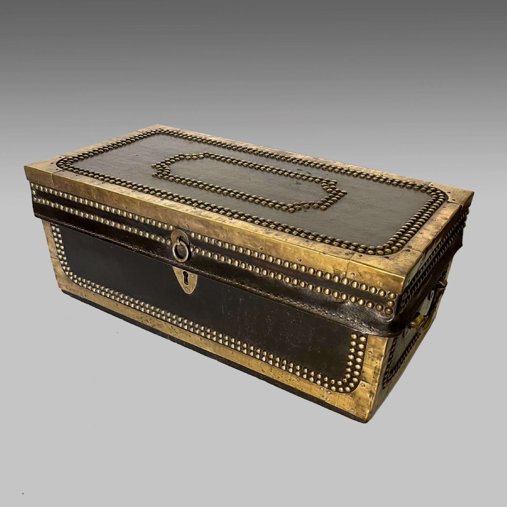 A dark brown leather-covered rectangular camphor trunk embellished with decorative brass studding, brass corner mounts, and a central brass lock plate.