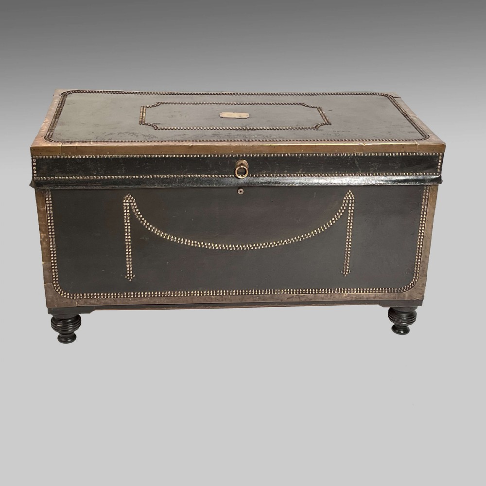 A rectangular dark leather-covered trunk with brass studding in swag and border designs, raised on turned wooden feet.