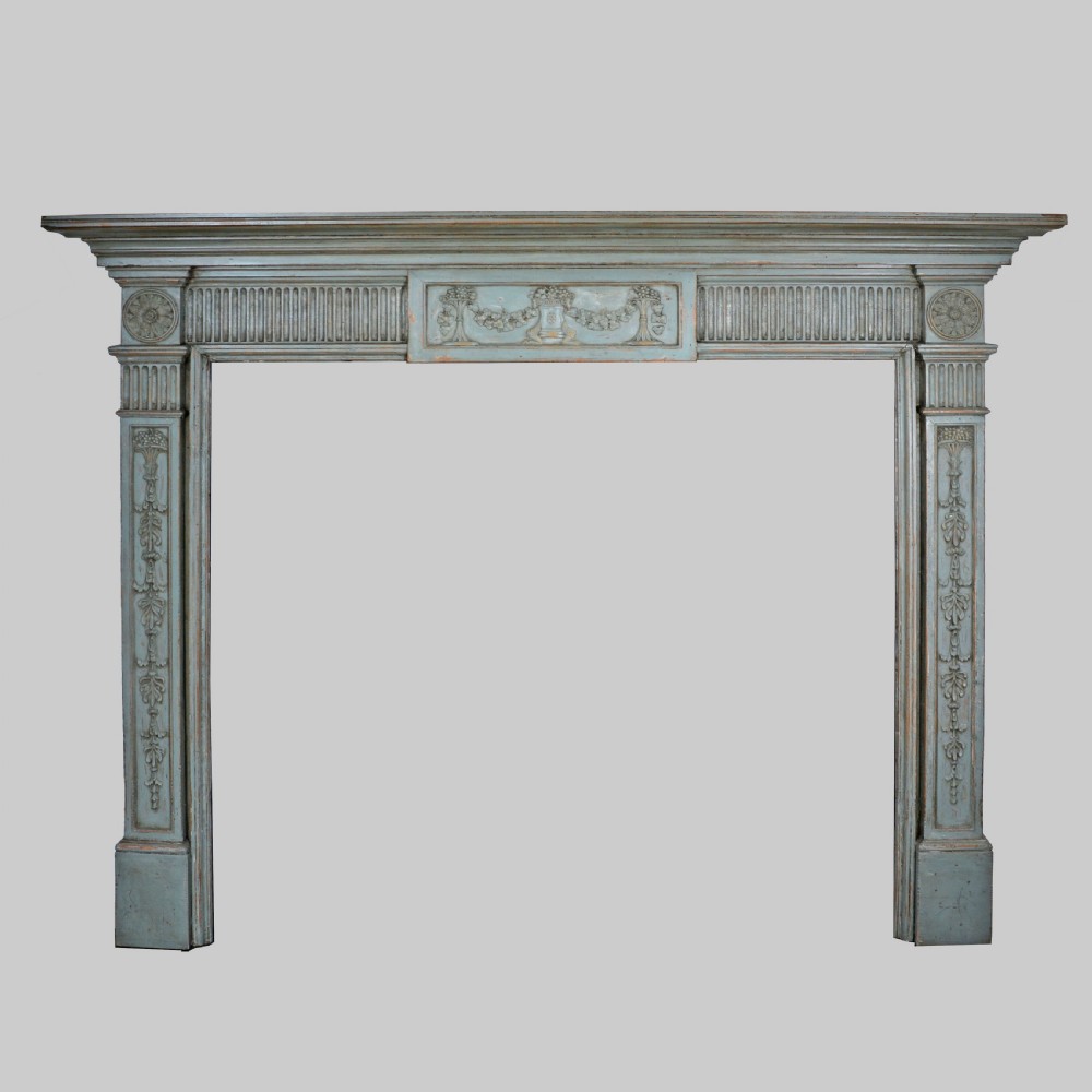 A carved Georgian Neoclassical fire surround painted pale blue, featuring fluted pilasters, decorative festoons, and a central urn panel.