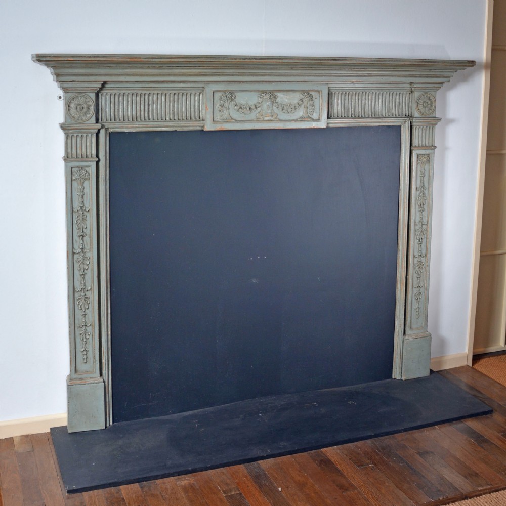 A carved Georgian Neoclassical fire surround painted pale blue, featuring fluted pilasters, decorative festoons, and a central urn panel. View II
