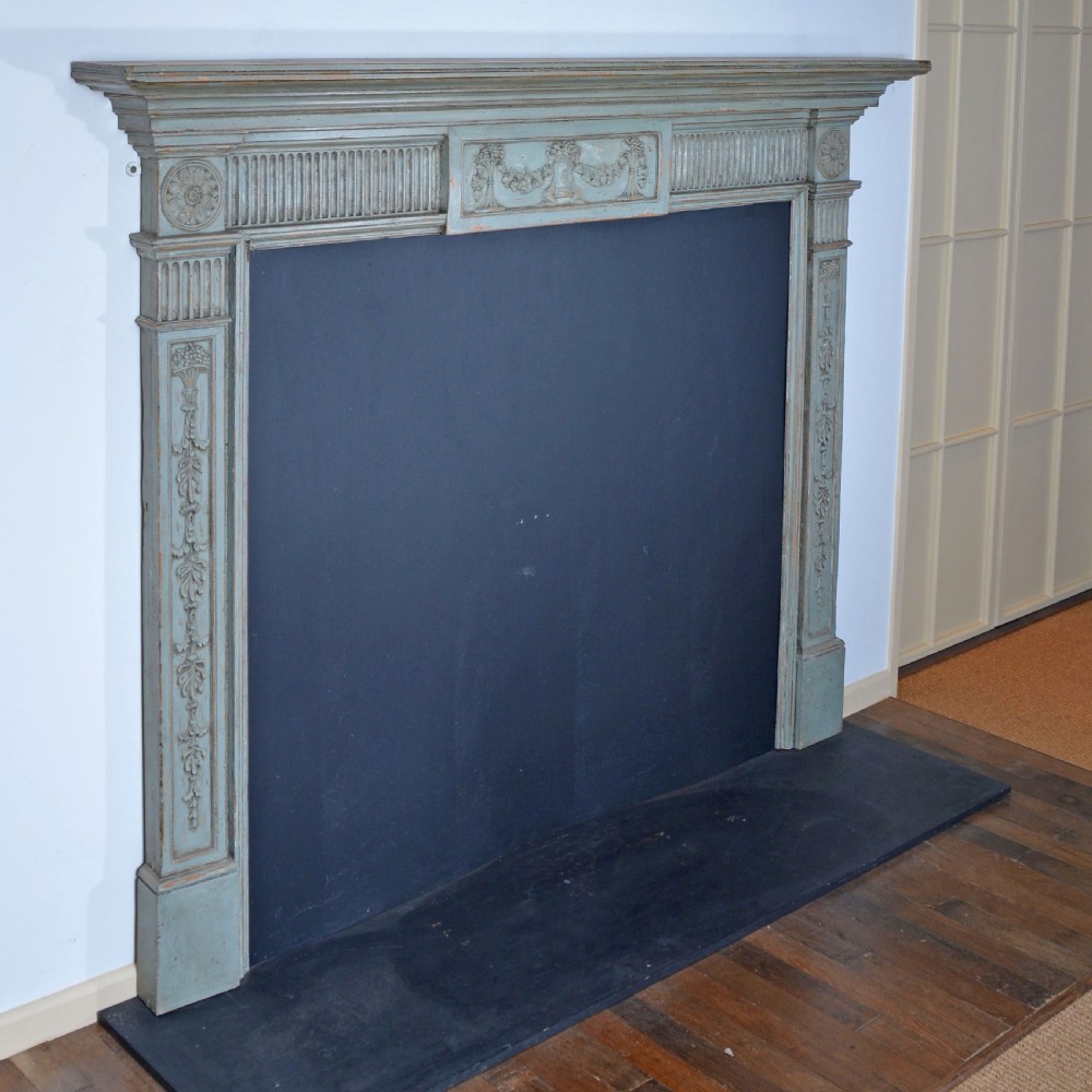 A carved Georgian Neoclassical fire surround painted pale blue, featuring fluted pilasters, decorative festoons, and a central urn panel. View III
