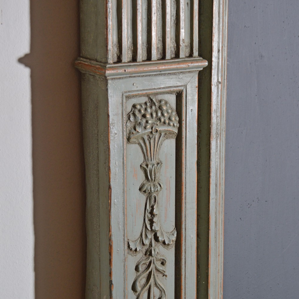 A carved Georgian Neoclassical fire surround painted pale blue, featuring fluted pilasters, decorative festoons, and a central urn panel. View IV