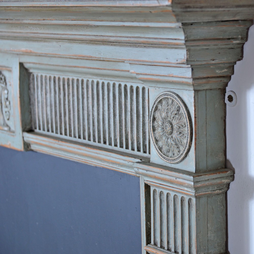 A carved Georgian Neoclassical fire surround painted pale blue, featuring fluted pilasters, decorative festoons, and a central urn panel. View V